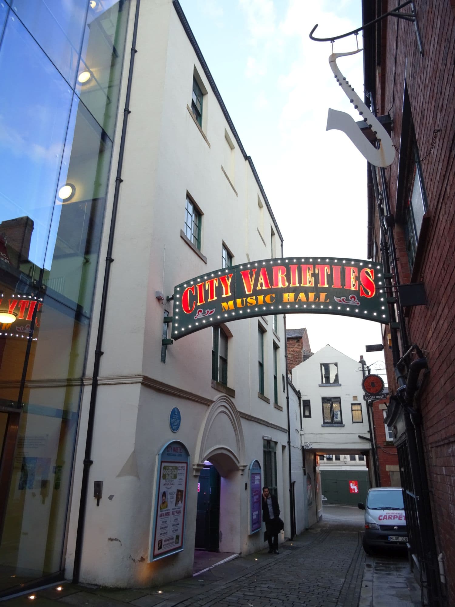 Illuminated City Varieties Music Hall sign arching over a cobbled Leeds alley beside a saxophone-shaped sign