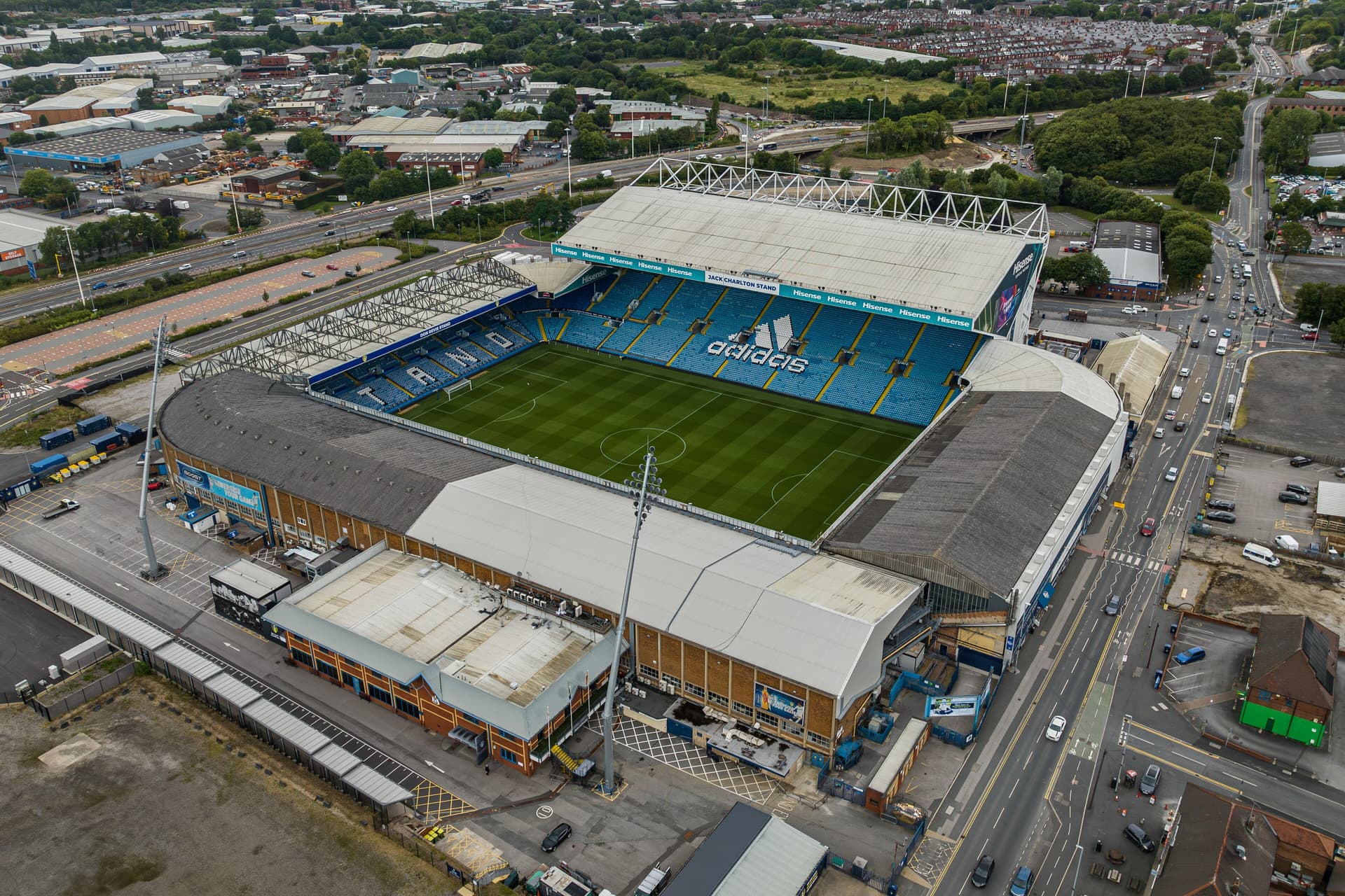 Aerial view of a football stadium with blue seats, green pitch, floodlight mast and surrounding roads and industrial units
