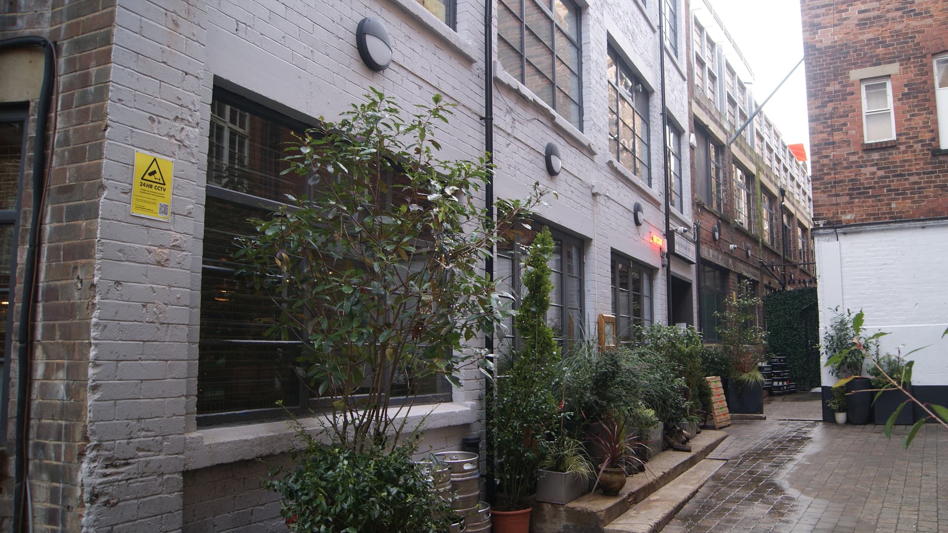 Narrow cobbled Leeds yard with painted brick warehouse frontage, planted pots, steel beer kegs and a Headrow House sign