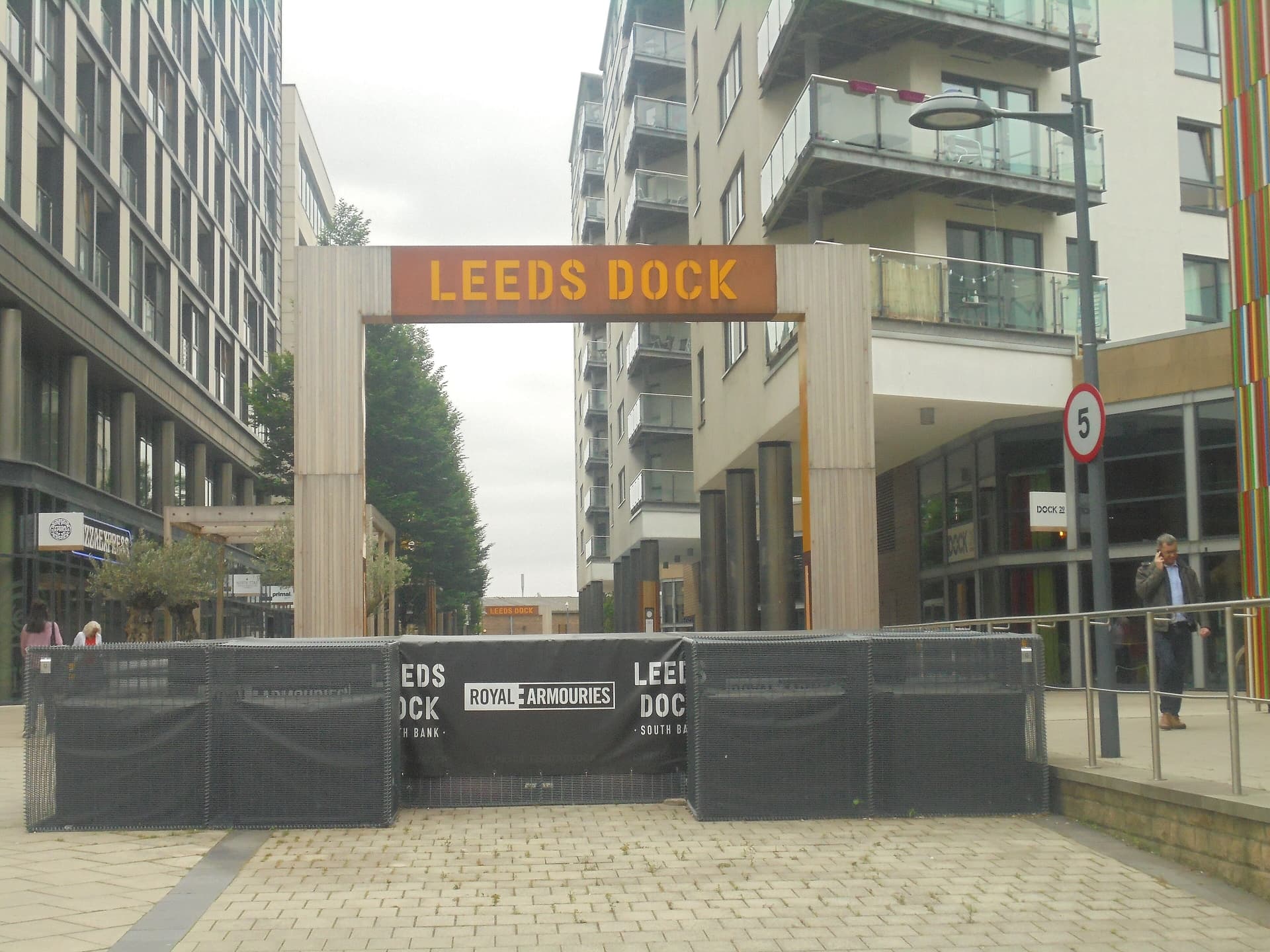 Rusty metal Leeds Dock archway over a paved pedestrian street lined with modern apartment blocks