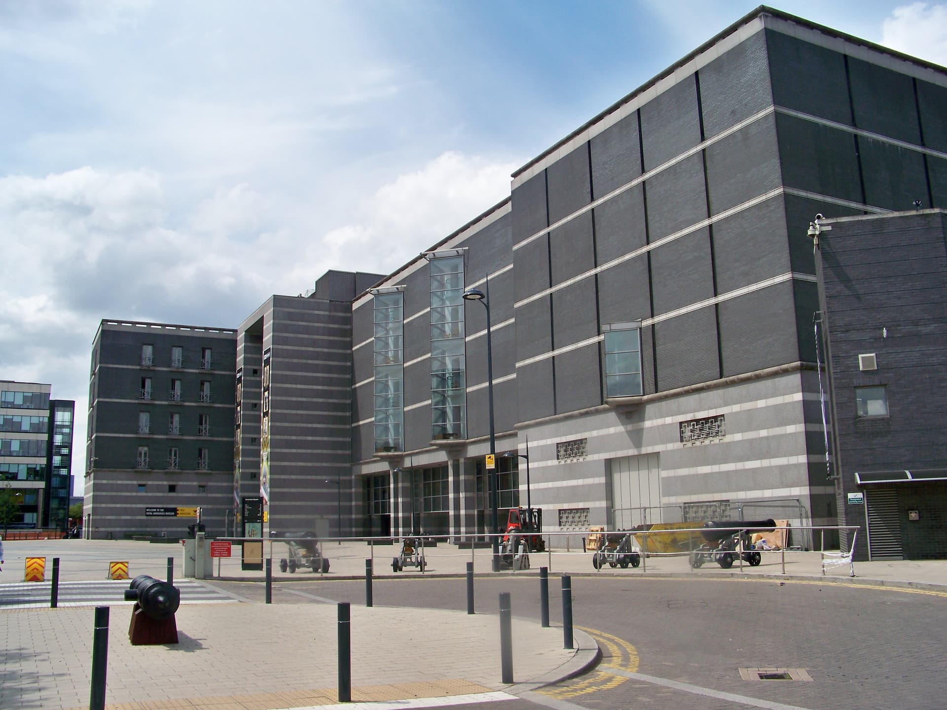 Dark brick and granite exterior of the Royal Armouries museum in Leeds, with cannons displayed on the square in front