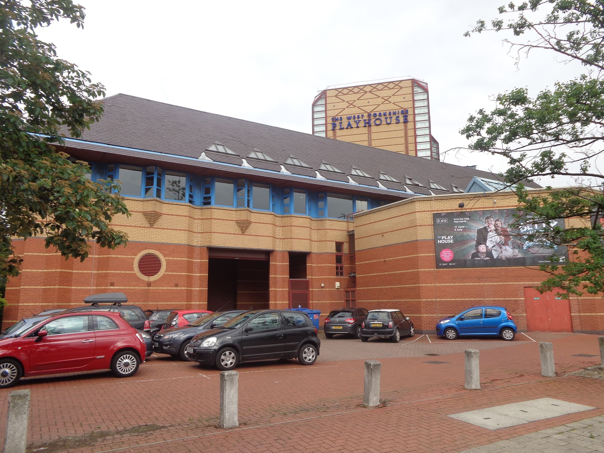 Red and yellow brick West Yorkshire Playhouse building in Leeds with tower sign and cars parked in front